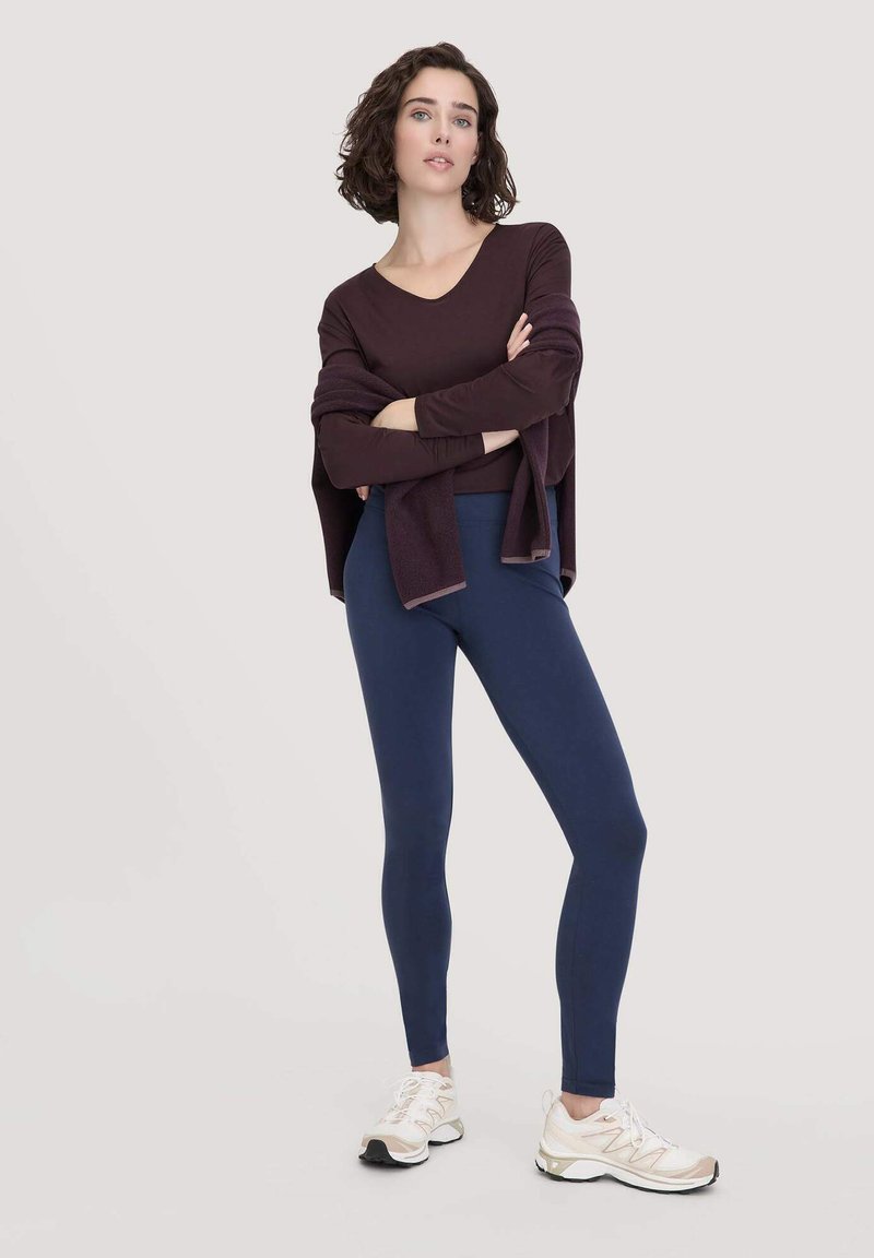 Sportliches Outfit mit einem tiefpurpurnen Langarmshirt und navyblauen Leggings. Vervollständigt mit weißen und grauen Sportschuhen. Glatte Textur.