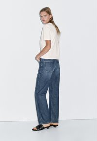 Gräddfärgad t-shirt med kort ärm, högmidjade blå denimjeans, vida ben, klassisk design, svarta sandaler med öppen tå, minimalistisk stil.