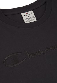 Mørkeblå bomulds T-shirt med et broderet "Champion" logo i en mørkere grå farve. Rund halsudskæring og korte ærmer med en glat struktur.