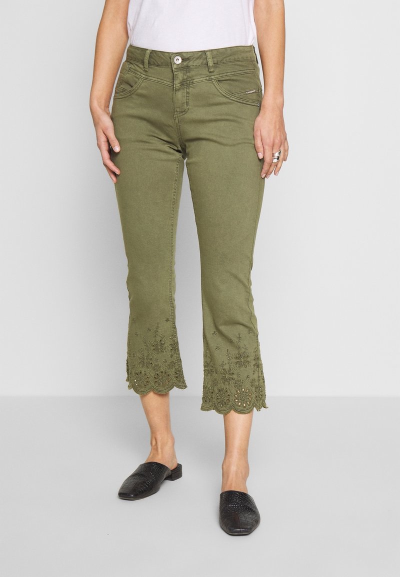 Olive green cropped jeans with scalloped, embroidered hem detailing. Made of denim fabric, featuring front pockets and a zip closure.