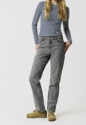 Rento asu, jossa on tummansiniraidallinen pitkähihaisena paita, harmaat korkeavyötäröiset farkut ja vaaleanruskeat kengät, joissa on pehmustettu pohja.