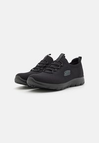 Zapatillas deportivas negras con un upper de malla transpirable, cordones elásticos y una suela de goma texturizada. Presenta el logo en el costado y una tira de agarre.
