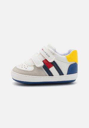 Biały sneaker z szarymi zamszowymi akcentami, niebieskim i żółtym obcasem oraz czerwono-niebieskimi paskami. Posiada rzepy i perforowany wzór na czubku buta.