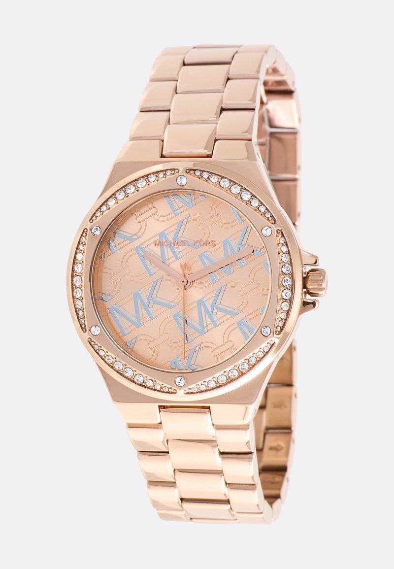 Montre en métal rose doré avec un cadran rond, des accents en cristal et un cadran en rose doré à motifs, mettant en avant des lettres bleues et un design de maillons.