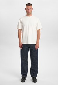 T-shirt bianca in cotone con collo girocollo e maniche corte, abbinata a jeans di denim blu scuro. Scarpe nere completano l'outfit.