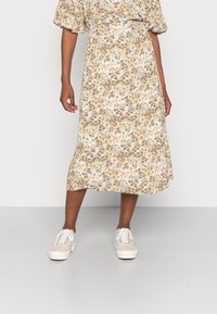 Robe midi fleurie à manches courtes bouffantes, avec un motif beige, marron et vert. Associée à des baskets légères. Texture de tissu lisse.