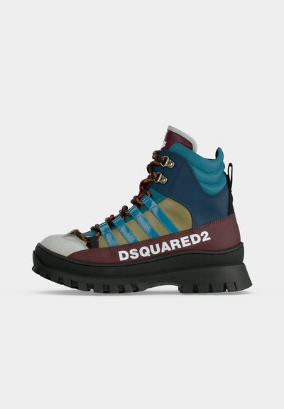 Botte de randonnée haute avec semelle noire épaisse, côtés bleu et olive, accents bordeaux, lacets orange et marquage "DSQUARED2" sur le côté.