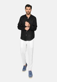 Camicia nera di lino, pantaloni bianchi di lino, scarpe espadrillas blu. Dettagli notevoli: parte anteriore con bottoni, maniche arrotolate, vestibilità rilassata.
