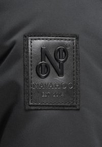 Patch in pelle nera con logo che presenta "NAVAHOO" e "EST 2014", cucito su un tessuto scuro con una texture liscia e un leggero lucido.