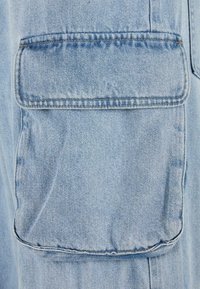 Lys blå denimstof med en stor flaplomme på den øverste side, synlige sømme og blød tekstur. Ideel til afslappet brug.