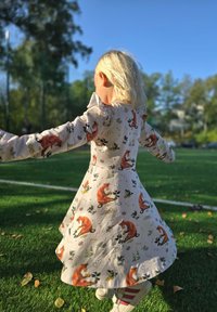 Vaaleanvärinen, pitkähihaista mekko, jossa on punaisen kettujen ja kasvien kuvio. Vaahtomainen muotoilu, käytetty valkoisten kenkien päällä, joissa on punaiset raidat.