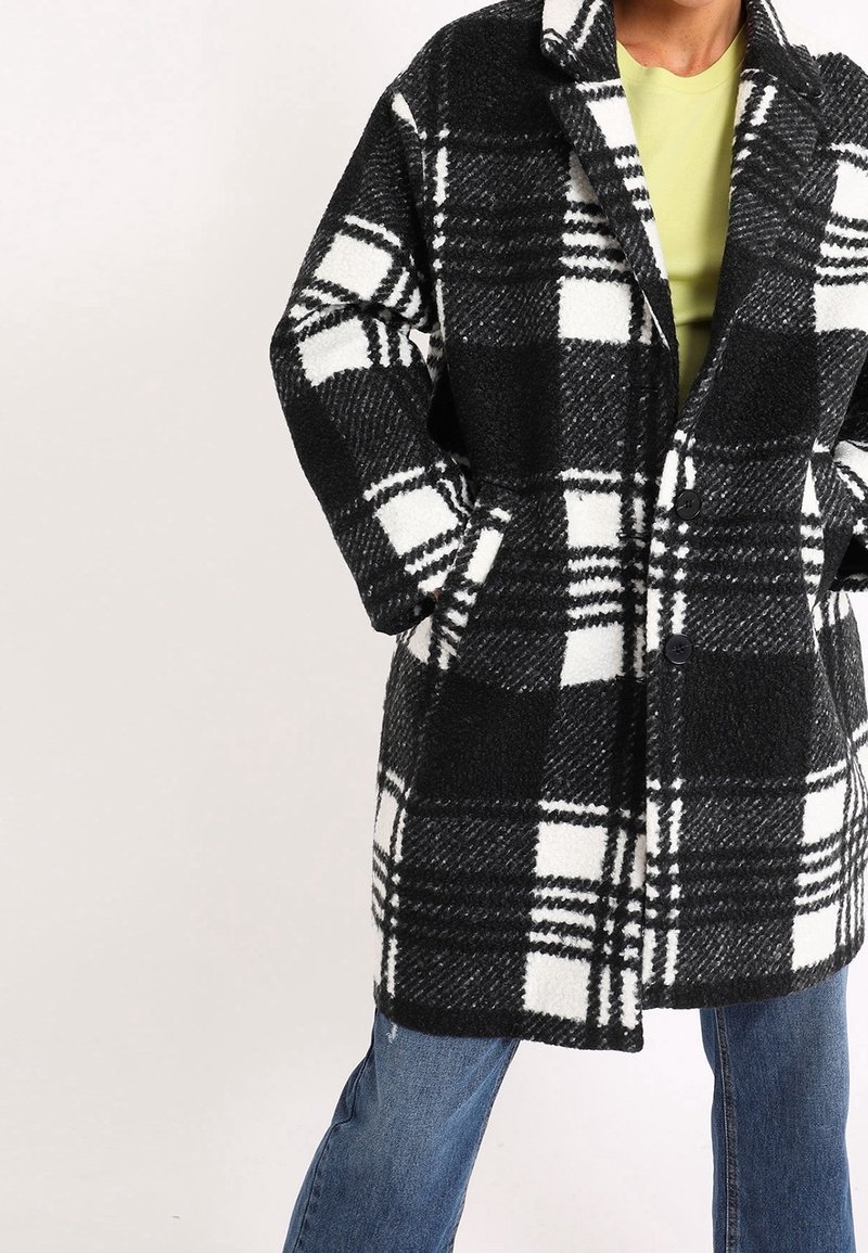 Cappotto a quadri bianco e nero in misto lana con maniche lunghe, tasche frontali e colletto a rever. Abbinato a jeans in denim blu.