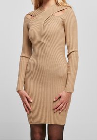 Abito beige aderente a coste con maniche lunghe, caratterizzato da un design con ritagli asimmetrici sulle spalle e una texture liscia.