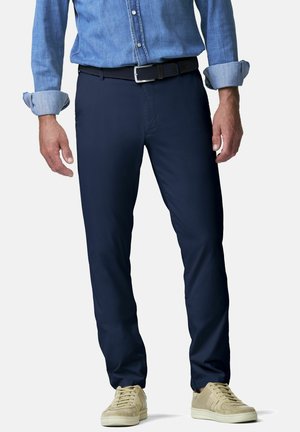 Mann trägt dunkelblaue Slim-Fit-Hose, schwarzen geflochtenen Gürtel, hellbraune Turnschuhe und ein hellblaues, hochgekrempeltes Jeanshemd.