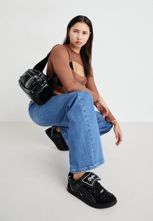 Zwarte schoudertas met meerdere ritszakken, bruine blouse met lange mouwen met een uitsnijdingen ontwerp, en blauwe wijde jeans met rafelige zoom.
