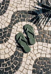 Tongs verts sur un pavement en mosaïque de pierre blanche et noire avec des ombres partielles de feuilles de palmier au-dessus.