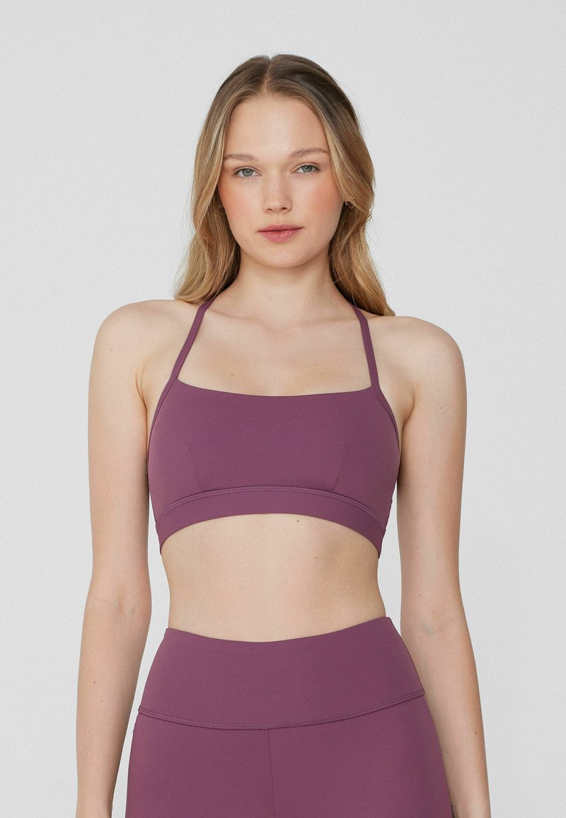 Lila sportlicher Crop-Top mit verstellbaren Trägern, glatter Textur, geradem Ausschnitt und einem kontrastierenden Gummibund am unteren Ende.
