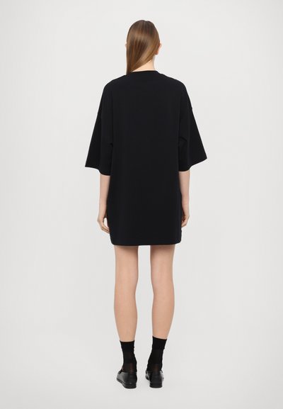 Överdimensionerad svart T-shirtklänning med korta ärmar, rund hals och rak skärning som slutar ovanför knäet; tillverkad av mjukt bomullstyg.