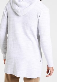 Lysegrå, tekstureret hættetrøje med lang pasform, sideslids og afslappet pasform. Fremstillet af vævet stof.