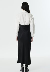 Camisa blanca con mangas abullonadas, superpuesta a un vestido de satén negro. El vestido es ajustado, llega hasta los tobillos y tiene una textura suave.