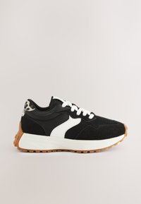 Zapatilla deportiva negra con detalles en blanco, materiales de malla y ante, suela de goma y un detalle de estampado de leopardo en el talón.