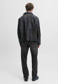 Chaqueta de cuero negra con un acabado mate, que presenta un corte relajado y un gran cuello, combinada con jeans gris oscuro y zapatos negros.
