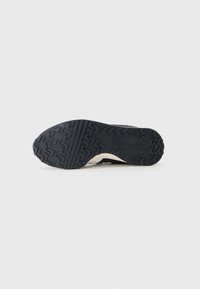 Zwarte rubberen zool met een getextureerd loopvlakpatroon. Heeft een witte tussenzool en een donkere bovenkant, ontworpen voor grip en duurzaamheid.