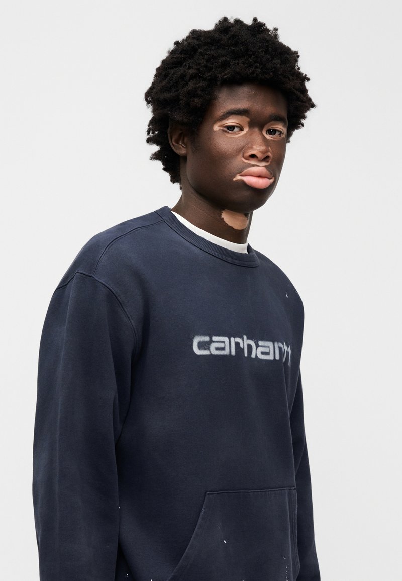 Marineblauer Pullover mit einer Vordertasche und grauem "carhartt"-Logo. Verfügt über einen klassischen Rundhalsausschnitt und ein weiches, strukturiertes Gewebe.