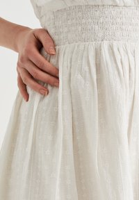 Robe blanche présentant une taille smockée texturée, de délicats motifs brodés et des plis fluides, mettant en valeur un tissu léger et une finition douce.