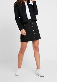 Černá džínová bunda, bílé tričko, černá mini sukně z umělé semiše se stříbrnými patentními knoflíky a bílé tenisky. Jednoduchý a moderní outfit.