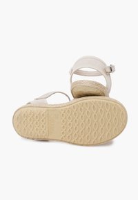 Beige sandalen met een gestructureerd bandontwerp, enkelband met gesp en een geweven zool met een golfpatroon. Zool gemarkeerd met "Made in Spain."