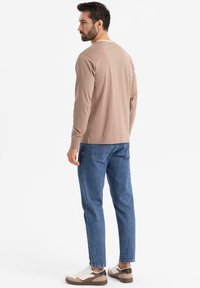 Beige Langarmhemd, Denim-Jeans und Sneakers. Einfaches Design mit Rundhalsausschnitt und gerade geschnittenen Hosen. Weicher Stoff.