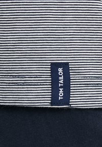 Tessuto blu navy con strisce orizzontali bianche; presenta un'etichetta tessuta con la scritta "TOM TAILOR" in testo bianco su sfondo blu navy.