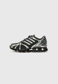 Chaussures de sport noires avec une tige en maille, des accents argent métallisé, plusieurs rayures et une semelle distinctive rembourrée avec des sections circulaires.