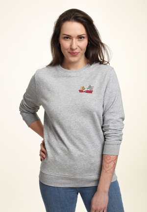 Felpa grigia realizzata in morbido tessuto, con un logo colorato di "Tom e Jerry" sul petto. Maniche lunghe con polsini e orlo a costine.