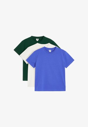 Trois t-shirts à manches courtes et col rond, pliés en bleu, blanc et vert foncé, empilés sur un fond blanc.
