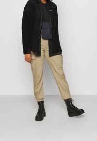 Černá kordurová košile s bundou, černá košile na knoflíky, béžové cargo kalhoty a černé platformové šněrovací boty. Malá námořnická ramenní taška.