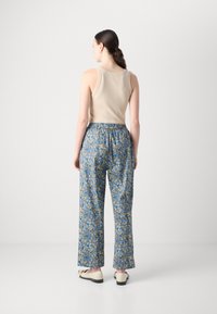 Top in beige e pantaloni a stampa floreale blu. I pantaloni presentano una vita elastica e una vestibilità ampia, con intricati motivi floreali e un tessuto morbido.