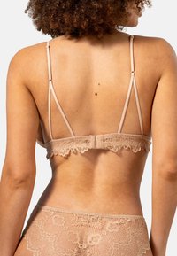 Nude bh med spetskanter, justerbara remmar och hak-och-ögon-stängning, med en slät textur och delikat blommönster.