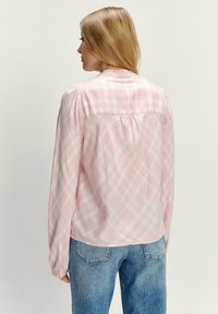Lichtroze geruite blouse met lange mouwen en een relaxed fit, achterkant met plooidetail en zachte, gestructureerde stof, gecombineerd met vervaagde blauwe jeans.