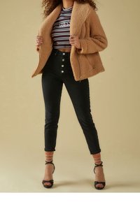 Tan faux fur -turkis jakku, jossa on vetoketjukiinnitys, raidallinen crop-top, korkeat mustat farkut, joissa on nappiyksityiskohtia, ja mustat remmikenkiä.