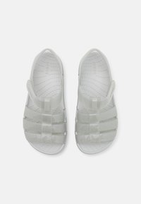 Světle šedé sandály Crocs s průhledným designem, obsahující čtyři široké pásky a zadní pásek pro bezpečné nošení, texturovaná stélka pro pohodlí.