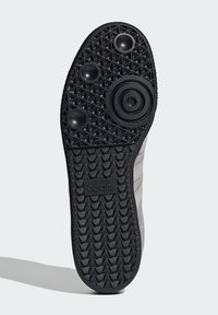 Suela de zapato de goma negra con patrón texturizado, elementos de diseño circular y logo de Adidas. Presenta una banda de rodadura prominente y puntos de tracción.
