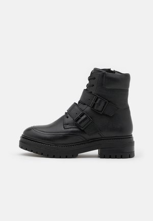 Bottine noire en cuir avec deux brides réglables à boucle, fermeture à lacets à l'avant et semelle épaisse crantée.
