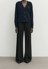 Cardigan côtelé marine avec un col en V et une fermeture à boutons, associé à un pantalon noir à jambes larges, créant une silhouette ample.
