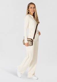 Weißes, geripptes Langarmshirt kombiniert mit cremefarbenen, weit geschnittenen Hose mit hoher Taille und weißen Sneakers. Braune Umhängetasche mit gemusterten Akzenten.