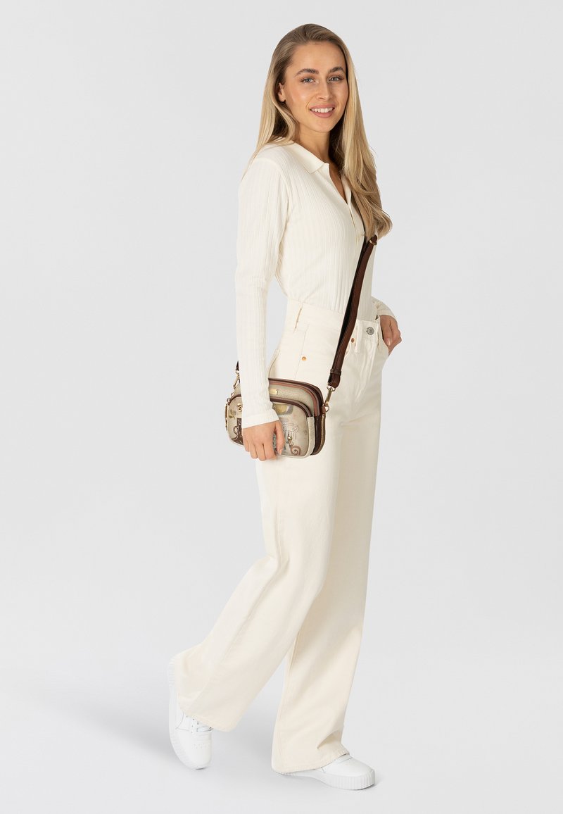 Weißes, geripptes Langarmshirt kombiniert mit cremefarbenen, weit geschnittenen Hose mit hoher Taille und weißen Sneakers. Braune Umhängetasche mit gemusterten Akzenten.