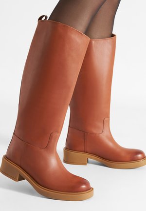 Hellbraune kniehohe Lederstiefel mit glatter Oberfläche, Blockabsätzen und einem dezenten Nahtdetail oben. Gummisohlen für besseren Halt und Langlebigkeit.