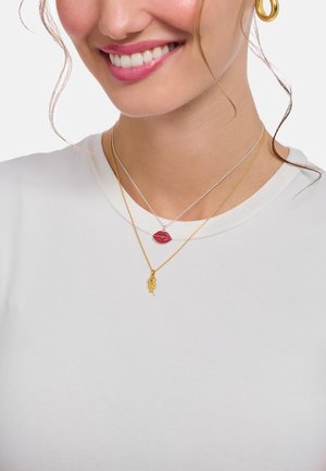 Layered necklaces featuring a red lips charm and a gold rose charm, showcased with a white shirt against a neutral background.