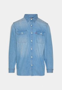 Chemise en denim bleu clair à manches longues, fermeture par boutons, deux poches poitrine et col classique. Présente un léger délavage et des coutures apparentes.
